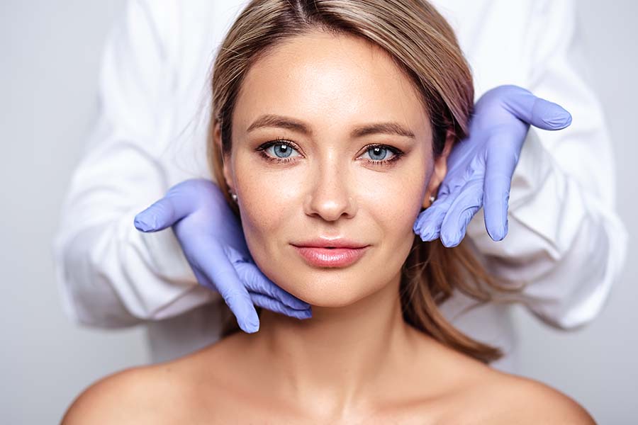 Close up portrait of young blonde woman with cosmetologyst hands in a gloves