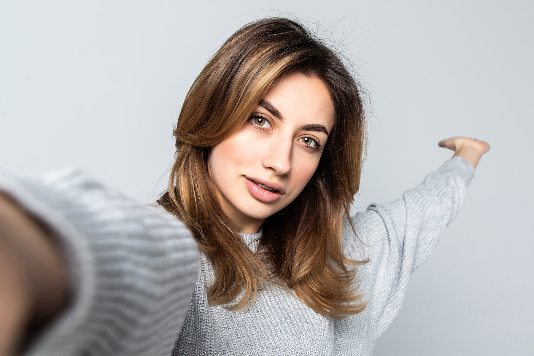 Young woman taking a selfie, wearing a grey sweater and presenting space to the side.