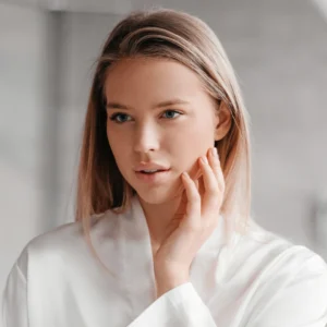 Woman with clear skin touching face in soft natural light, minimalist beauty portrait